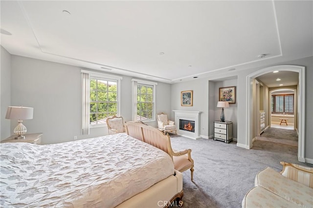 carpeted bedroom with baseboards, a glass covered fireplace, and arched walkways