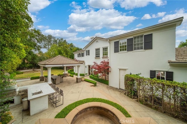 rear view of property featuring a gazebo, outdoor dry bar, and stucco siding