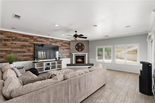 living room with a warm lit fireplace, recessed lighting, crown molding, visible vents, and ceiling fan