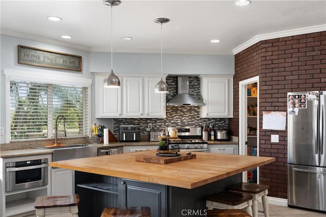 kitchen with wall chimney range hood, white cabinetry, wood counters, and stainless steel appliances
