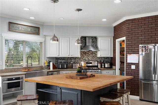 14445 Dove Canyon Dr, Riverside, CA 92503 - kitchen featuring appliances with stainless steel finishes, butcher block countertops, wall chimney range hood, white cabinets, and ornamental molding