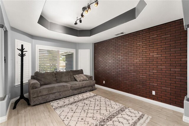 14445 Dove Canyon Dr, Riverside, CA 92503 - living room featuring brick wall, baseboards, light wood finished floors, a tray ceiling, and track lighting