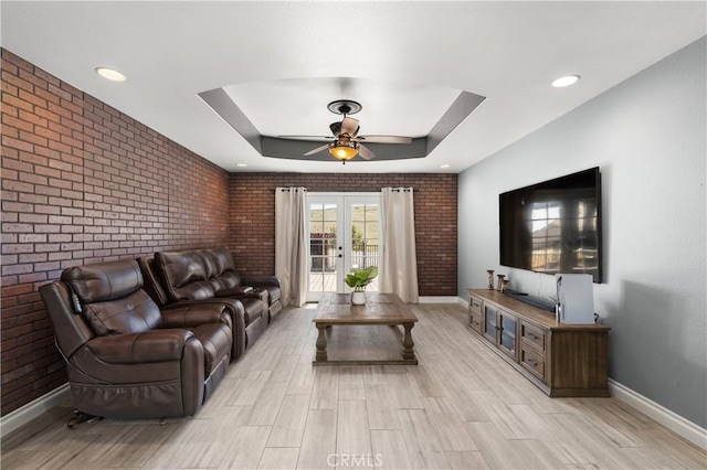 living room with a raised ceiling, brick wall, baseboards, and a ceiling fan