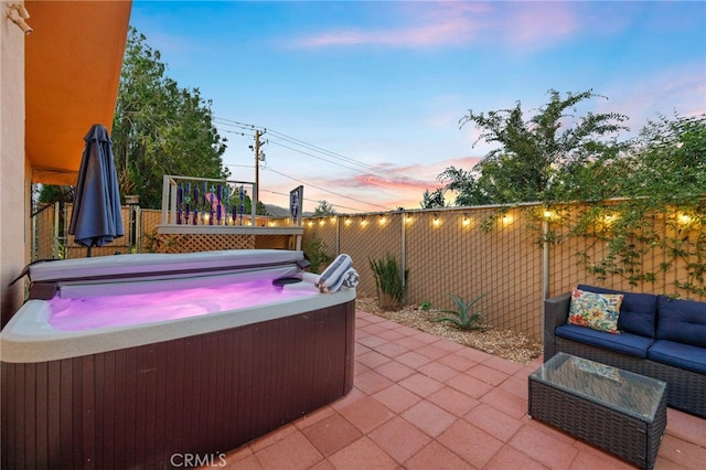 patio terrace at dusk featuring a hot tub, a fenced backyard, and outdoor lounge area