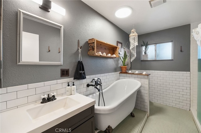 full bathroom with vanity, a freestanding tub, tile walls, a wainscoted wall, and visible vents