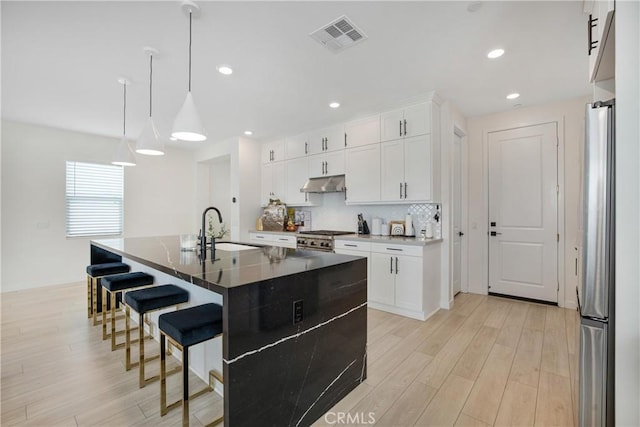 27824 Marquee Dr, Valencia, CA 91381 - kitchen with under cabinet range hood, light wood-type flooring, a breakfast bar, decorative backsplash, and stainless steel appliances
