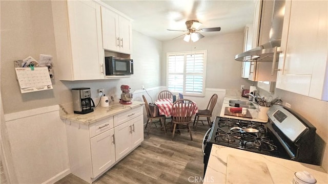 kitchen featuring ceiling fan, wood finished floors, a sink, gas range, and white cabinetry