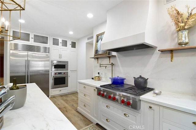 29528 Ridgeway Dr, Agoura Hills, CA 91301 - kitchen with appliances with stainless steel finishes, custom exhaust hood, white cabinetry, light wood-style floors, and glass insert cabinets