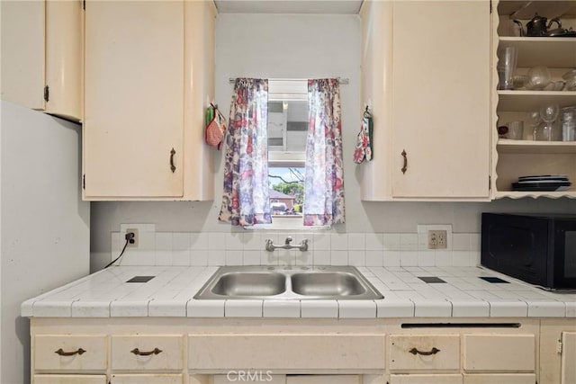 kitchen with light countertops, black microwave, freestanding refrigerator, and a sink