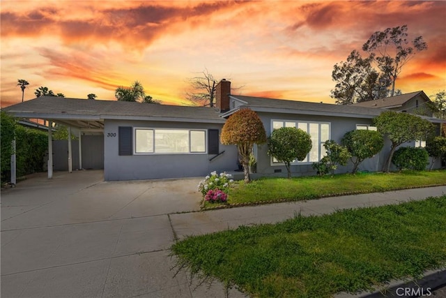 ranch-style home featuring stucco siding, a chimney, driveway, an attached carport, and a lawn