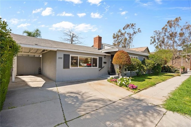 ranch-style home with stucco siding, a carport, a front lawn, a chimney, and driveway
