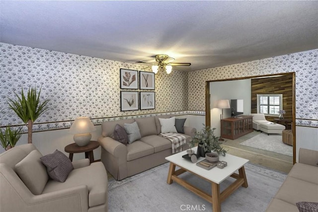 living area featuring a ceiling fan, wallpapered walls, and a textured ceiling