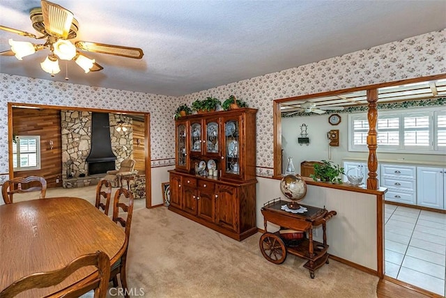 dining room featuring a textured ceiling, wallpapered walls, a ceiling fan, and light colored carpet