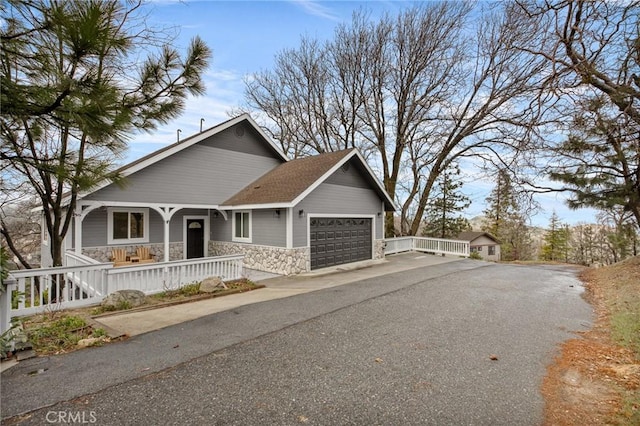 1207 Grass Valley Rd, Lake Arrowhead, CA 92352 - view of front facade featuring stone siding, covered porch, an attached garage, driveway, and roof with shingles