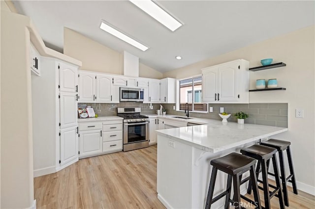 kitchen featuring white cabinetry, lofted ceiling, a sink, a peninsula, and appliances with stainless steel finishes