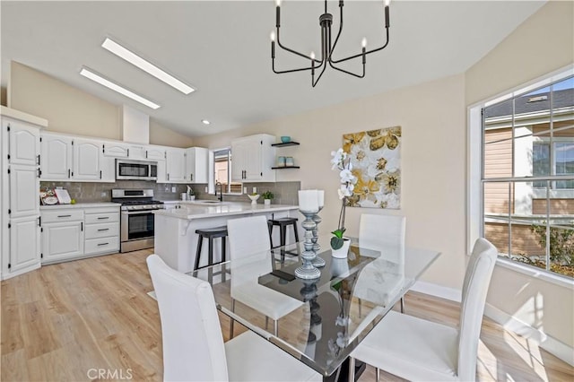 dining space with lofted ceiling with skylight, baseboards, a chandelier, and light wood-type flooring