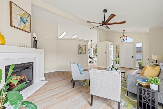 living room featuring wood finished floors, lofted ceiling, a high end fireplace, baseboards, and ceiling fan with notable chandelier