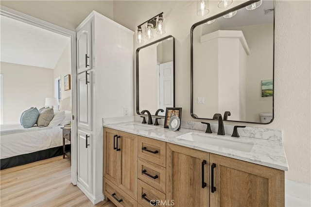 bathroom with ensuite bathroom, double vanity, wood finished floors, and a sink