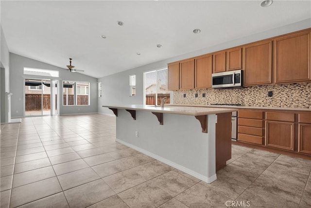 13204 Monrovia St, Hesperia, CA 92344 - kitchen with light countertops, backsplash, stainless steel microwave, a ceiling fan, and brown cabinetry