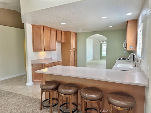 27813 Hummingbird Ln, Helendale, CA 92342 - kitchen with light countertops, a peninsula, brown cabinetry, gas stove, and arched walkways