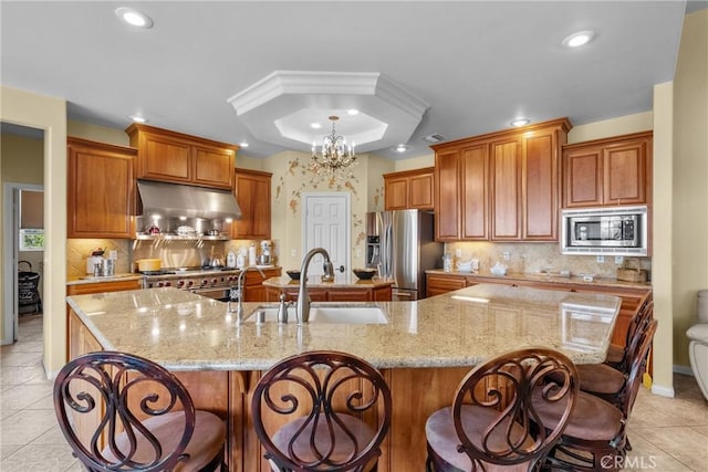 1403 Sonora St, San Bernardino, CA 92404 - kitchen featuring a large island with sink, a tray ceiling, under cabinet range hood, a sink, and appliances with stainless steel finishes