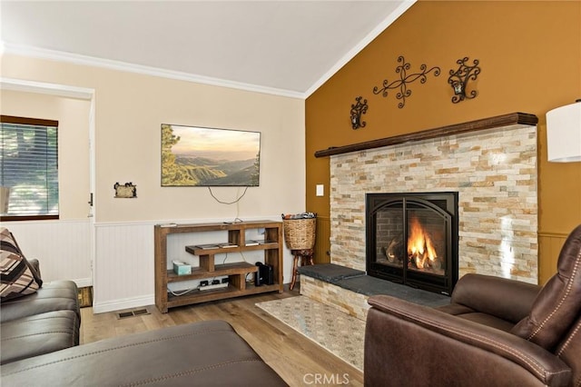 living area featuring crown molding, a wainscoted wall, visible vents, a stone fireplace, and wood finished floors