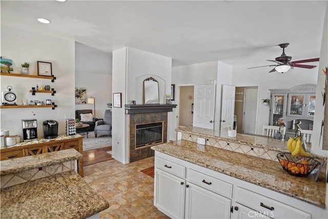 kitchen with white cabinetry, light stone counters, a ceiling fan, and a tile fireplace