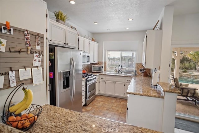 kitchen with white cabinets, a peninsula, light stone countertops, backsplash, and stainless steel appliances