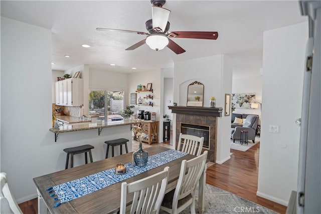 dining space featuring wood finished floors, baseboards, a ceiling fan, and a tile fireplace