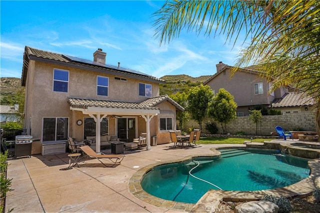 back of property with a patio, stucco siding, a chimney, a fenced backyard, and roof mounted solar panels