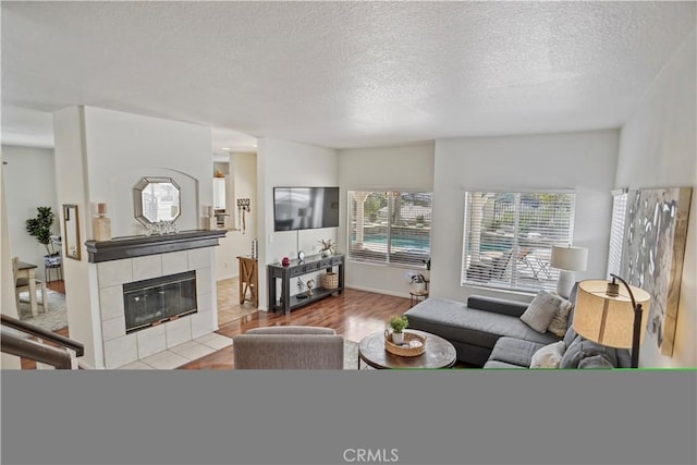 living room with a tiled fireplace, a textured ceiling, and wood finished floors