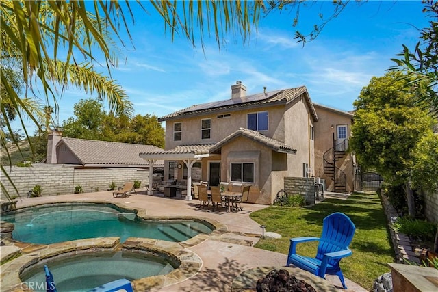 back of property with stucco siding, a chimney, an in ground hot tub, a patio area, and roof mounted solar panels