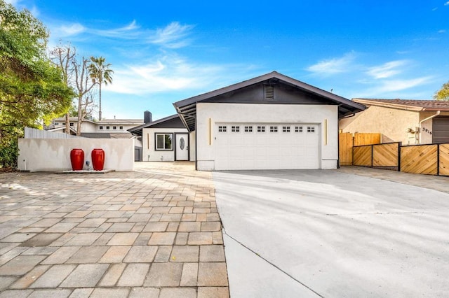 view of front facade with a gate, fence, decorative driveway, a garage, and stucco siding
