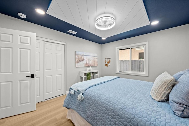 bedroom featuring a tray ceiling, a closet, wooden ceiling, visible vents, and light wood-style floors