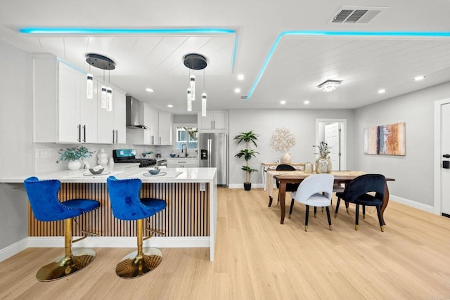 kitchen featuring light countertops, white cabinets, a peninsula, appliances with stainless steel finishes, and wall chimney exhaust hood