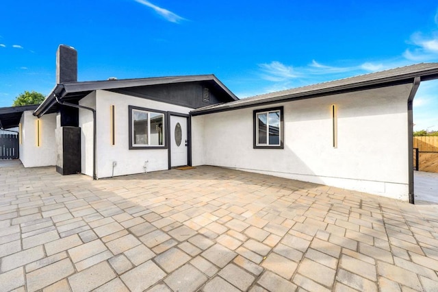 rear view of property featuring stucco siding, a chimney, fence, and a patio