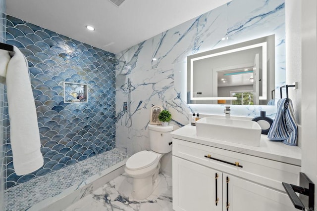 bathroom featuring toilet, tiled shower, vanity, marble finish floor, and tile walls