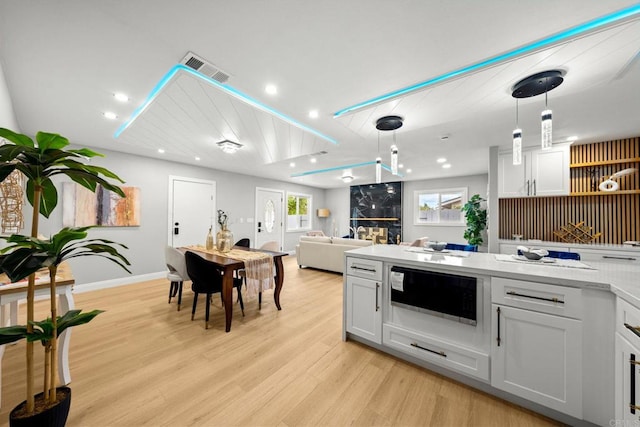 kitchen with white cabinetry, light countertops, decorative light fixtures, light wood finished floors, and visible vents