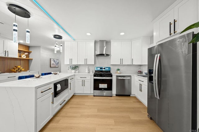 kitchen featuring light wood-style flooring, a peninsula, wall chimney exhaust hood, appliances with stainless steel finishes, and white cabinetry