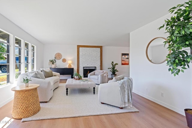living area with baseboards, wood finished floors, and a brick fireplace