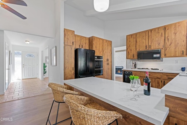 kitchen with brown cabinets, lofted ceiling with beams, black appliances, and ceiling fan