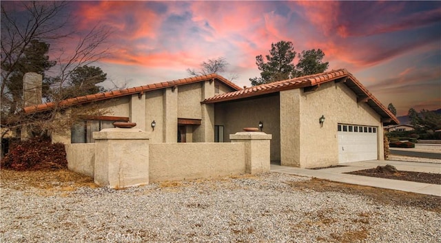 view of property exterior featuring stucco siding, fence, a tile roof, driveway, and an attached garage