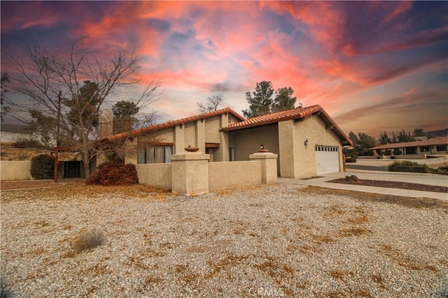 property exterior at dusk featuring a tile roof, stucco siding, a chimney, concrete driveway, and an attached garage