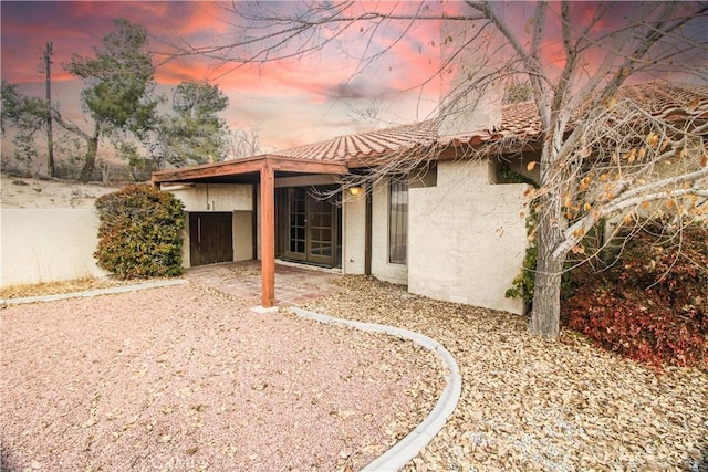 back of property at dusk with stucco siding, a tiled roof, and a patio