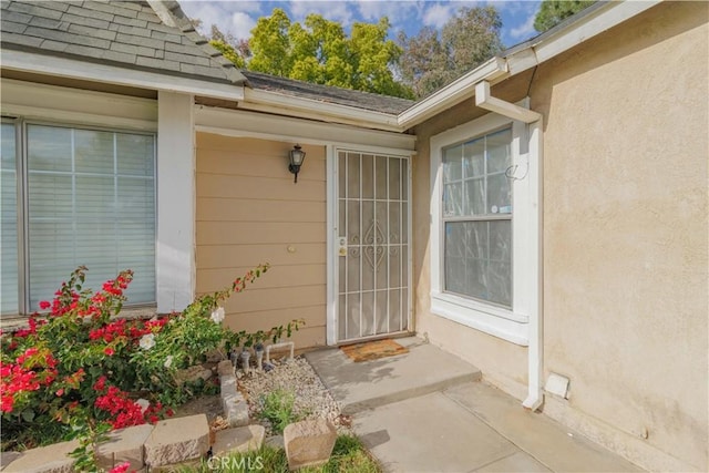 property entrance with stucco siding and roof with shingles