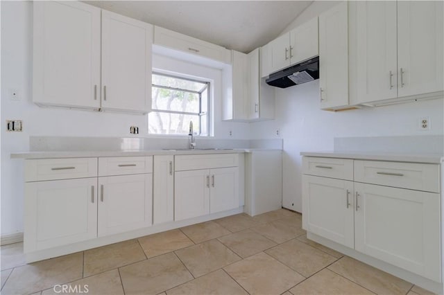 kitchen featuring light countertops, a sink, white cabinetry, under cabinet range hood, and light tile patterned floors