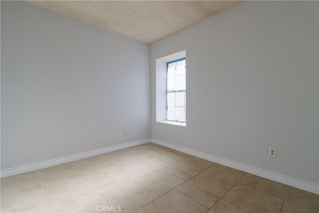 spare room featuring baseboards, a textured ceiling, and light tile patterned floors