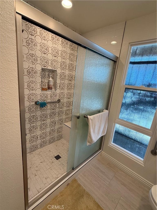 bathroom featuring toilet, a shower with door, wood finished floors, and baseboards