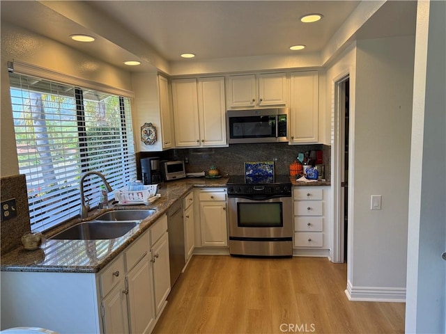 kitchen featuring white cabinets, light wood finished floors, stainless steel appliances, backsplash, and a sink