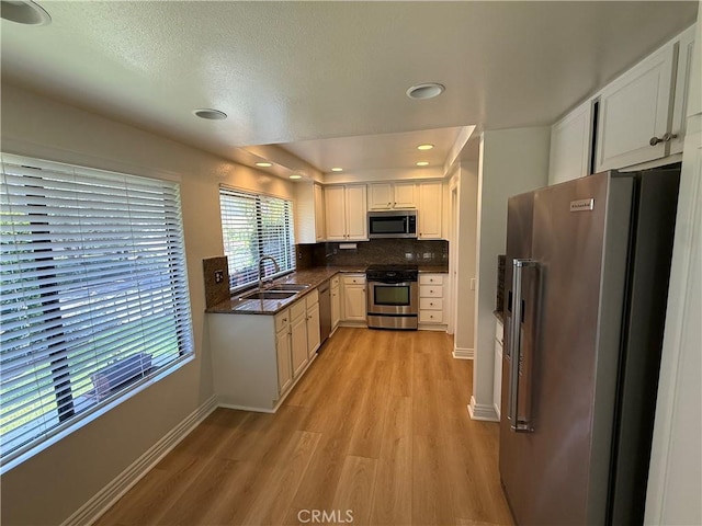 5219 Moya, Laguna Woods, CA 92637 - kitchen with stainless steel appliances, light wood-style flooring, dark countertops, white cabinetry, and backsplash